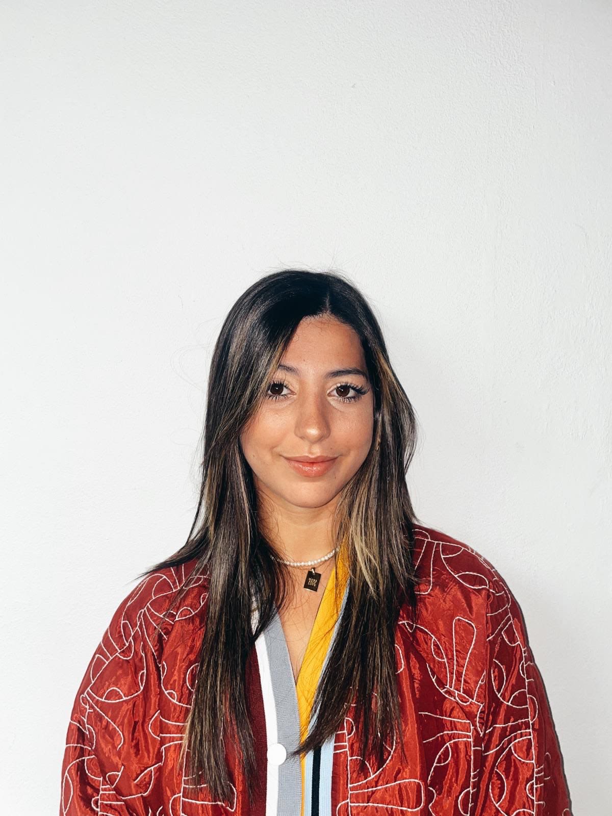 Retrato de Paola Díaz Álvarez mirando hacia la cámara. Se encuentra alfrente de una pared blanca. 