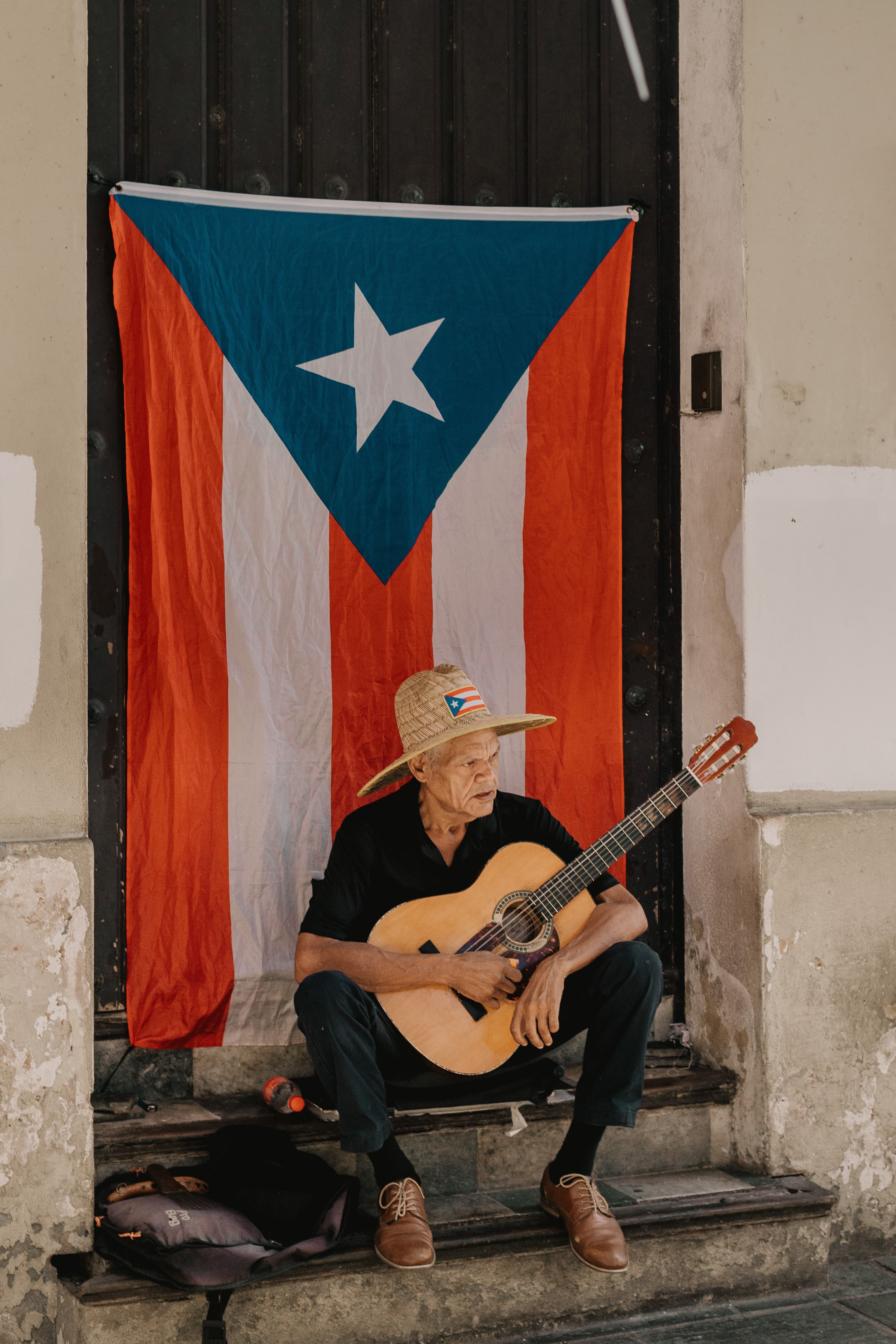 Hombre con una guitarra sentado frente a la bandera de Puerto Rico